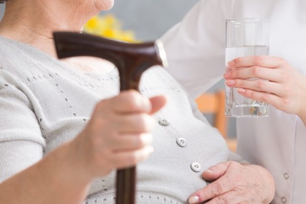 Elderly disabled woman and carer Elderly disabled woman with a walking stick and carer giving her glass of water